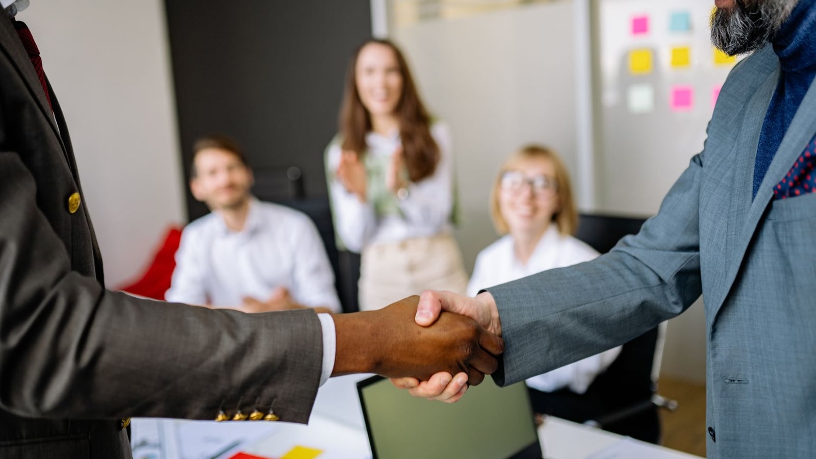 Two professionals shaking hands in a corporate lobby before an interview.